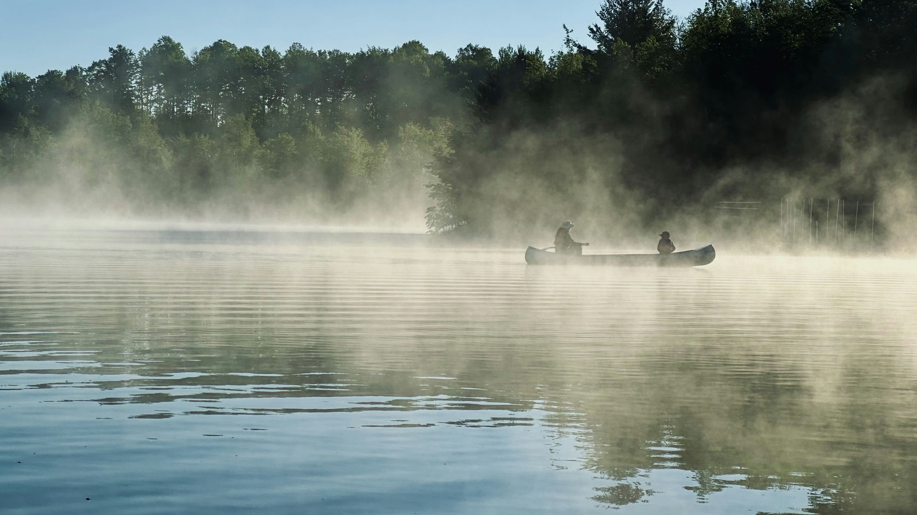 Mist rises off of Lake Killian as a canoe floats atop it, propelled by two scouts with rows